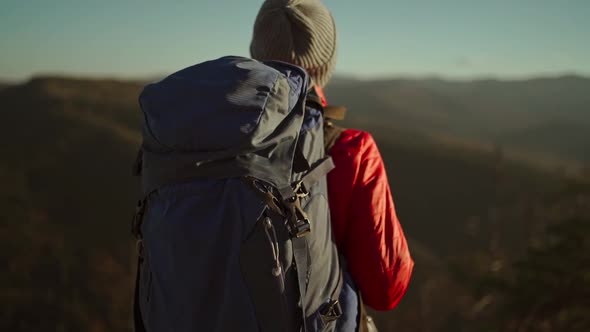 Slow Motion View From Behind Adventurous Female Hiker Backpacker in Red Jacket with Backpack Stands