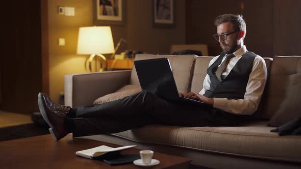 Young Businessman in Glasses Working at a Laptop, Man in the Suit Sitting on the Couch in the Hotel