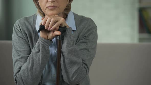 Old Woman Sitting on Couch, Holding Hands on Walking Stick, Looking Sad, Grief