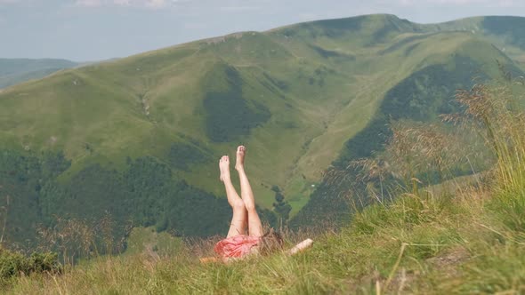 Young Woman with Long Slim Legs Lying Down on Green Meadow on a Warm Sunny Day in Summer Mountains