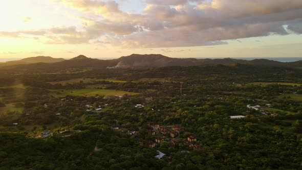 Aerial panement above a stunning mansion towering on a mountain ridge that is covered by thick tropi