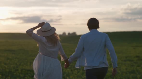 Sunset on a Countryside Young Couple in Nature Man and a Woman are Running Through a Field of