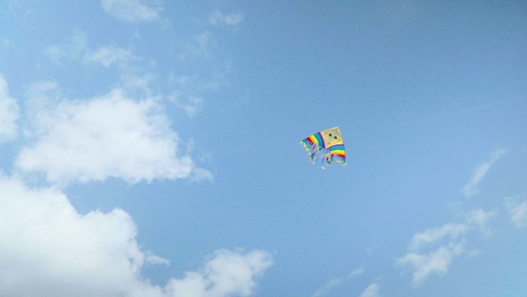 Colorful kite flying against the blue sky with clouds