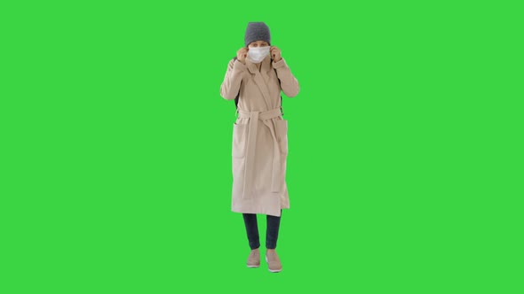 Woman Dressed in a Coat Wearing Putting on Protective Face Mask on a Green Screen, Chroma Key.