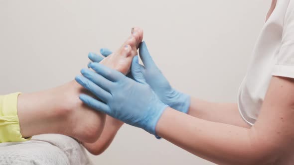 Podologist in blue medical gloves smears cream on a female's foot