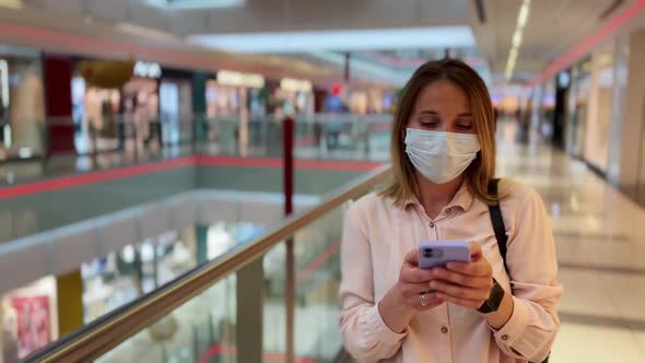Young Woman Wearing Medical Face Mask with Smartphone Looking Around Stores While Walking in Big