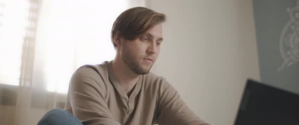 A close up of a young man sitting in bed and working on a computer. 