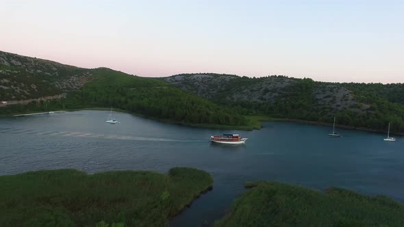 Aerial drone shot of a ferry in the river with sailboats anchored by the shore in Skradin in Šibenik