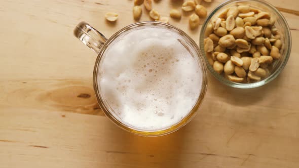 Top View of Beer with Foam and Salty Peanuts and on Wooden Table