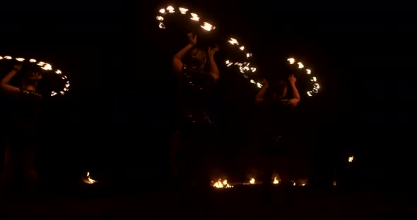 Three Women with Burning Hoops Dance with Fiery Torches in Leather Clothes in a Dark Hangar