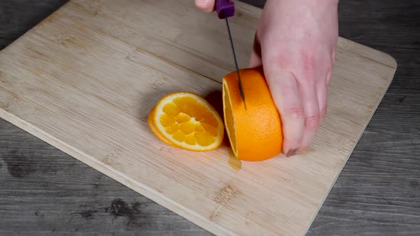 A woman in a kitchen cutting an orange on a wooden chopping board fruit salad