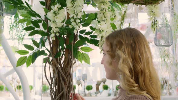 A Beautiful Woman with White Hair Touches the White Petals of Flowers in a Greenhouse