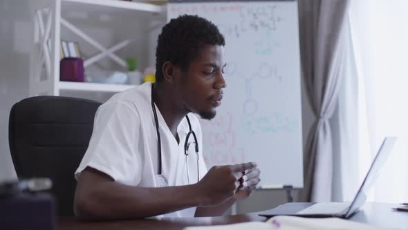 Side View Confident African American Scientist Conferencing Online Sitting at Table with Laptop with