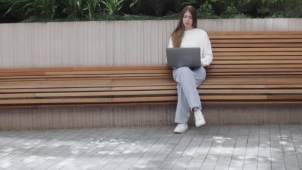 Young Female in Garden Using Laptop Communicates on Internet with Customer