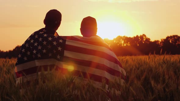 A Man and His Son Admire the Sunset Over a Field of Wheat, Wrapped in the Flag of the USA