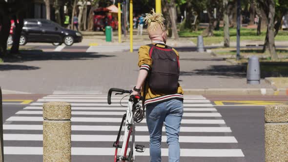 Albino african american man with dreadlocks crossing street with bike