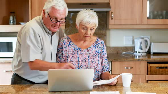 Senior couple calculating their bills on laptop in the kitchen