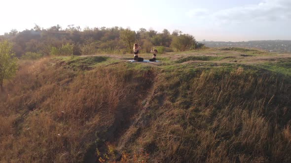 Aerial Drone View of Slender Young Mother Do Yoga Exercises with Child Daughter on High Hill By Lake