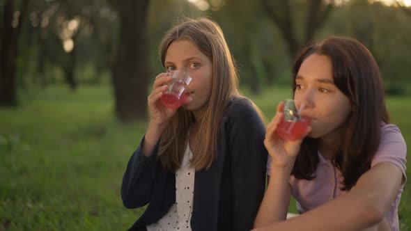 Two Carefree Teenage Girls Drinking Healthful Vitamin Juice in Slow Motion on Picnic in Park