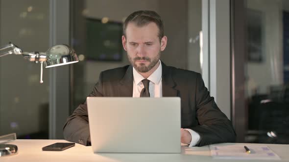 Serious Businessman Working on Laptop in Office at Night