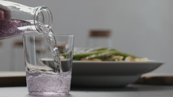 Slow Motion Pour Purple Fizzy Drink in a Tumbler Glass on Concrete Countertop with Pasta on