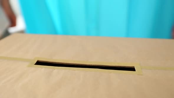 People put a paper ballot in a voting box at a polling station.