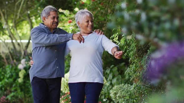 Video of happy biracial senior couple embracing and walking in garden