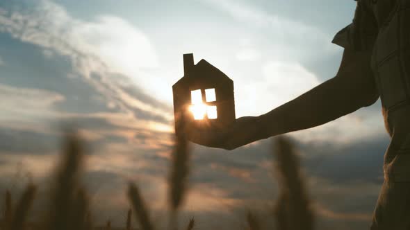 Silhouette Hand with Paper House at Sunset Background.