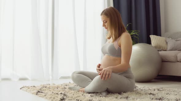 Pregnant Woman in Sportswear Sitting on the Carpet in the Lotus Position