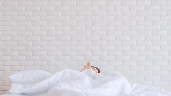 Woman stretching her arm after wake up on bed and looking outside windows