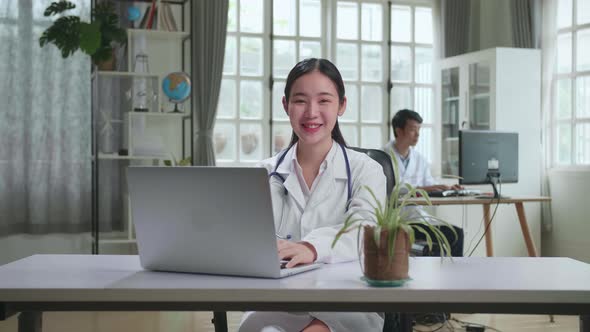 Young Asian Woman Doctor Is Using Laptop Computer And Smiling To Camera In Workplace