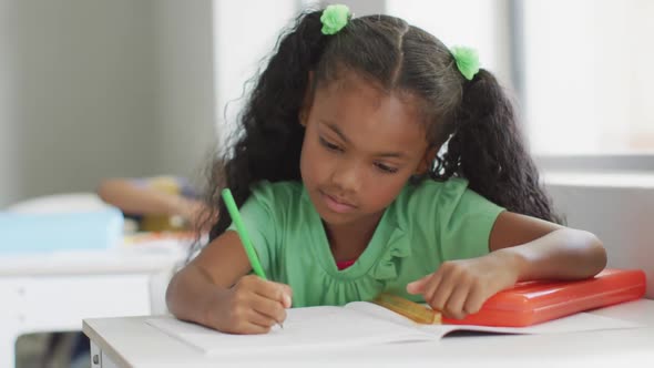 Video of african american girl sitting at desk during lesson in classroom