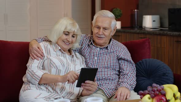 Senior Old Couple Grandparents Talking and Using Digital Tablet Computer at Home. Internet Shopping
