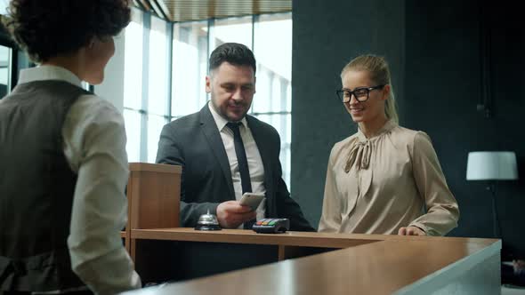 Young Couple Checkingin Hotel Talking To Receptionist Paying for Room with Smartphone Getting Key