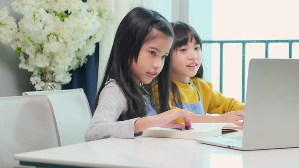 Two happy cute asian female children using laptop for remote education