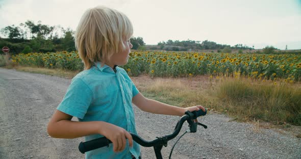 Children Looks to the Sunflower Meadow Stands with a Bicycle on Summer Vacation