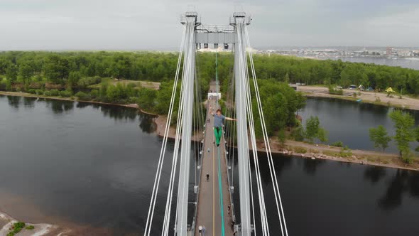 A Man Walks on a Rope Stretched Between the Supports of the Bridge at High Altitude. alt