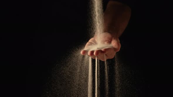 Stream of Dry Sand Pours Into Palm of Man and is Spilling Through His Fingers on Black Background