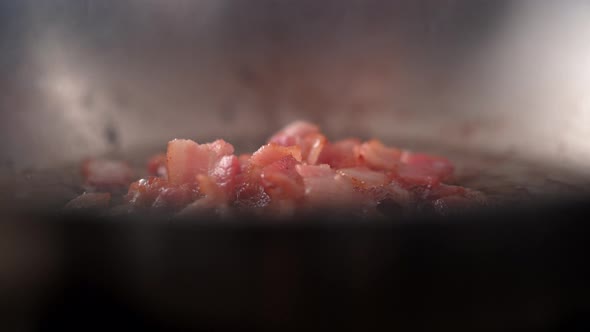 Camera follows adding chopped garlic on cooked bacon in a pan. Slow Motion.