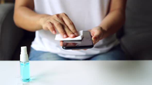 Young woman using alcohol spray for cleaning smartphone