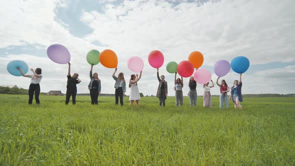 Cheerful Girls are Standing on the Field with Large Balloons and Colorful Balloons