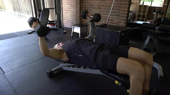 Tattooed man in home gym doing decline chest fly