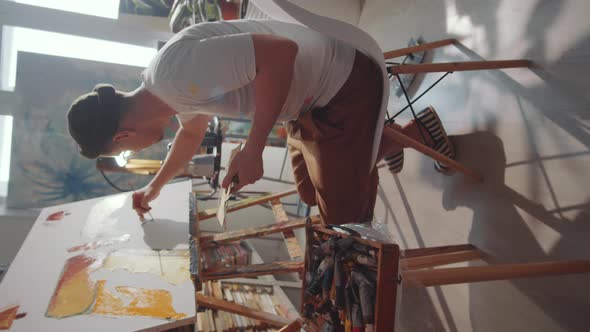 Young Male Artist Sitting on Chair and Painting in Art Studio