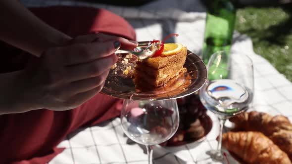 woman sits on cloth and eating cake at picnic in summer