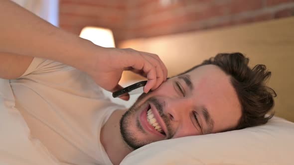 Portrait of Young Man Talking on Smartphone in Bed