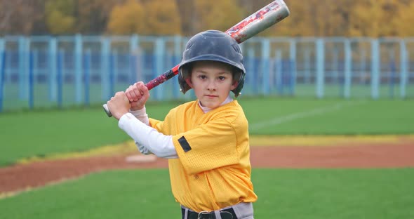 Portrait of a Boy Baseball Player on a Blurry Background, the Batter Holds a Baseball Bat in His