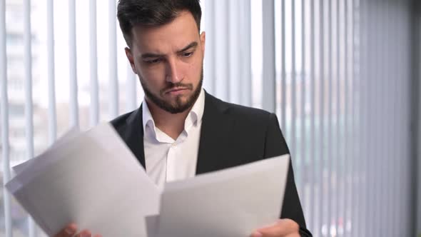 The camera zooms out of the face of a young manager, who is examining papers