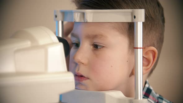 A Little Boy Having a Treatment in Eye Clinic - a Little Boy Looking Through the Lens in the Device