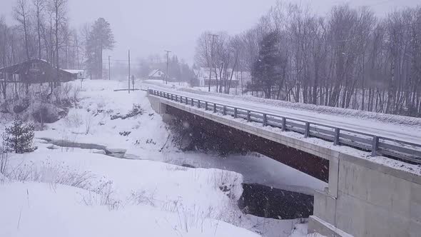 SLOW MOTION Aerial shot approaching a bridge corssing over an icy river during a snow storm