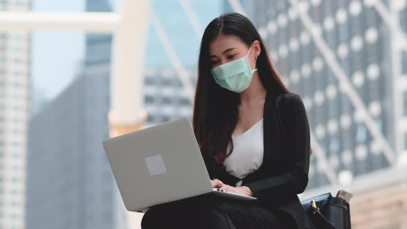 Business girl with mask use laptop outdoor with day light and she action of get good idea